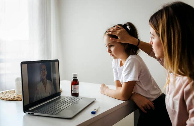 Mother checking daughter while attending video call with doctor over laptop at home model released Symbolfoto property released MGOF04699