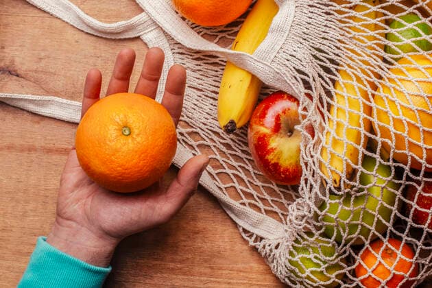 Reusable cotton mesh bag with fresh fruits and hand of man holding ripe orange model released Symbolfoto RTBF01597