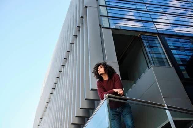 IMAGO Creative: Business - Progressive Geschäftsmodelle Young man leaning on railing while modern office building in background model released Symbolfoto AODF00379