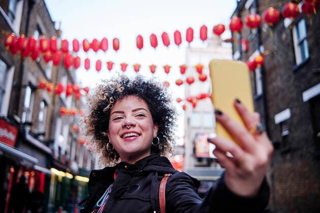 IMAGO Creative: Kollidierende Kulturen Smiling hipster woman taking selfie through smart phone at Chinatown model released Symbolfoto ASGF00183