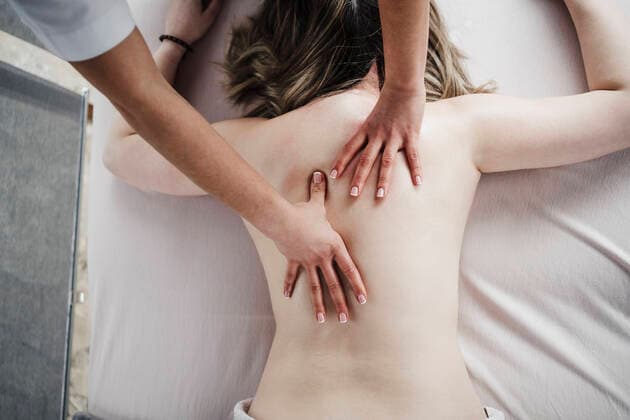 Female physical therapist massaging back of shirtless patient lying on front in hospital model released Symbolfoto property released EBBF03240