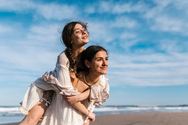 IMAGO Creative: Internationaler Frauenmonat, Gesundheit, Frauen in der Menopause Young woman looking away while piggybacking female friend at beach model released Symbolfoto EGAF02206