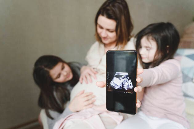 Curious daughter with mobile phone showing ultrasound embryo of baby at home model released Symbolfoto property released EYAF01567
