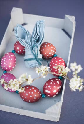 Blossoming twigs, napkin folded into shape of rabbit ears and wreath made of red spotted Easter eggs GISF00784