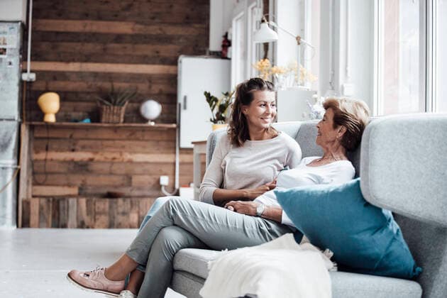 IMAGO Creative: Jahreszeit Winter, Couching Smiling young woman talking with grandmother while relaxing on sofa at home model released Symbolfoto property released GUSF05496