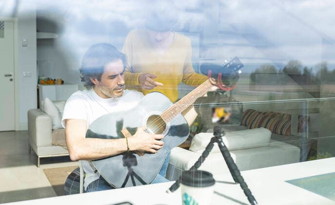 Woman discussing with man holding guitar while vlogging at home model released Symbolfoto property released JCCMF01615