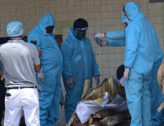 Family members in PPE perform last rights of a COVID-19 patient at a crematorium, in New Delhi, India, Tuesday, May 4, 2021. More than 20 million Indians have been infected with the coronavirus as it continues to spread with 3,500 deaths in the past 24 hours.  DEL2021050406 Abhishek
