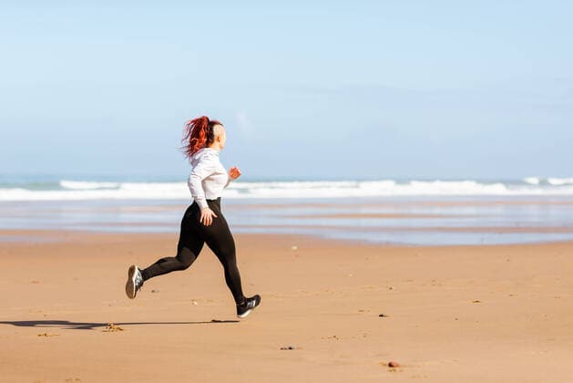 IMAGO Creative: Sport Dichotomien - Land und Wasser Side view of active female jogger running on ocean shore during training in summer, Model released Copyright: xAlbertoxMenendezx MR