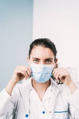 Creative Highlights Symbolbilder Young female medic putting on sterile mask while looking at camera in hospital on two color background during coronavirus pandemic, Model released Copyright: xAlvaroxSanchezx MR