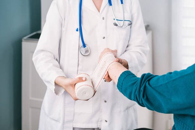 Crop anonymous doctor in uniform wrapping gauze around wrist of patient in hospital, Model released Copyright: xAlvaroxSanchezx MR