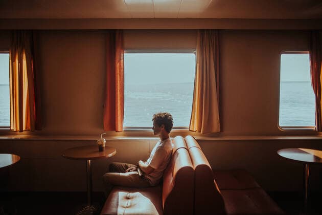 Side view thoughtful young male wearing casual summer clothes sitting on soft couch while travelling in ferry on rippling sea in Greece bright, Model released Copyright: xCamillexGirardx MR