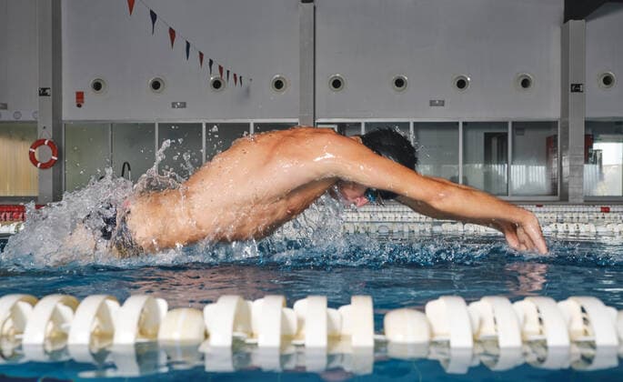 IMAGO Creative: Sport Dichotomien - Land und Wasser Side view of strong male swimmer in bathing cap performing butterfly stroke during workout in swimming pool with blue water, Model released, Property released Copyright: xCienxXxCienxStudiox MR