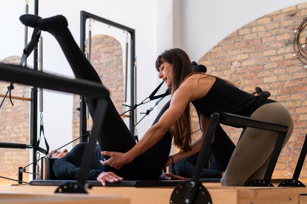 Flexible female stretching legs with help of personal instructor while doing exercises on pilates reformer, Model released Copyright: xEnriquexEspinosax MR