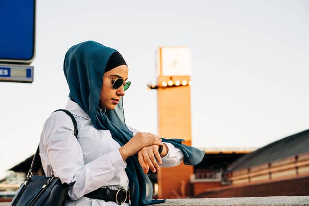 IMAGO Creative: Ruhe im Chaos IMAGO Creative: 2021 Favoriten Side view of Muslim female in hijab standing on platform at railway station and checking time on wristwatch while waiting for train Copyright: xJakexJakabx Model Released