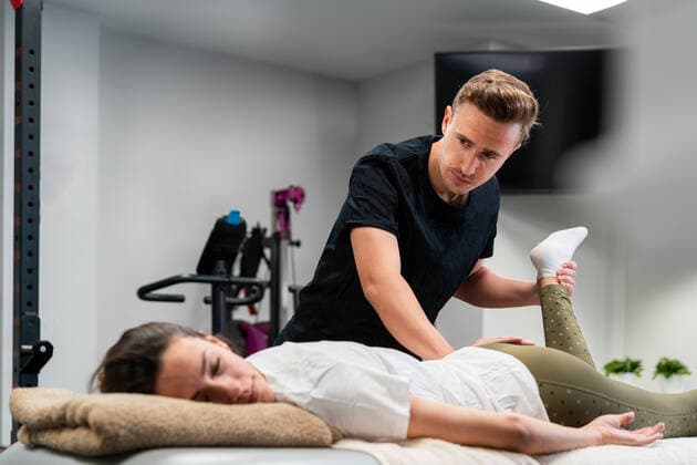 Adult male physiotherapist touching leg of woman with closed eyes during examination on bed in hospital, Model released Copyright: xEnriquexEspinosax MR