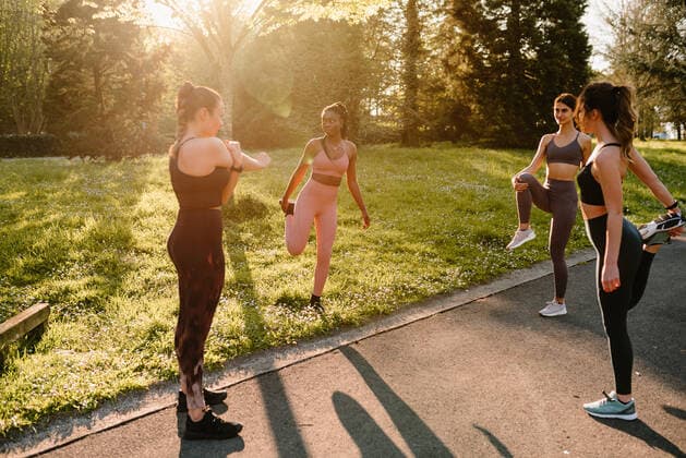 IMAGO Creative: Sommer, Sommertage im Stadtpark Young multiracial female athletes in sportswear stretching arm and legs on asphalt footpath in town on sunny day, Model released Copyright: xOierxAsox MR