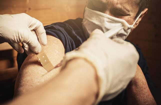 bavaria, germany - 01 may 2021: woman was vaccinated at home by a doctor during a home visit and receives a patch bandage from the nurse for the wound. Covid-19 Vaccination, Hausarzt