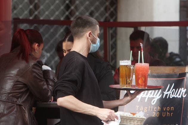 Due to persistently low incidences in Düsseldorf, catering establishments were allowed to reopen their outdoor areas if guests could show a negative coronal test A waiter wearing a mask carries a tray of drinks to one of the crowded tables in a bar in the Altstadt, North Rhine-Westphalia, Germany