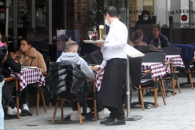 Due to persistently low incidence rates in Düsseldorf, catering establishments were allowed to reopen their outdoor areas if guests could show a negative coronary test A waiter at a restaurant in the Altstadt carries drinks on a tray to one of the crowded tables, North Rhine-Westphalia, Germany