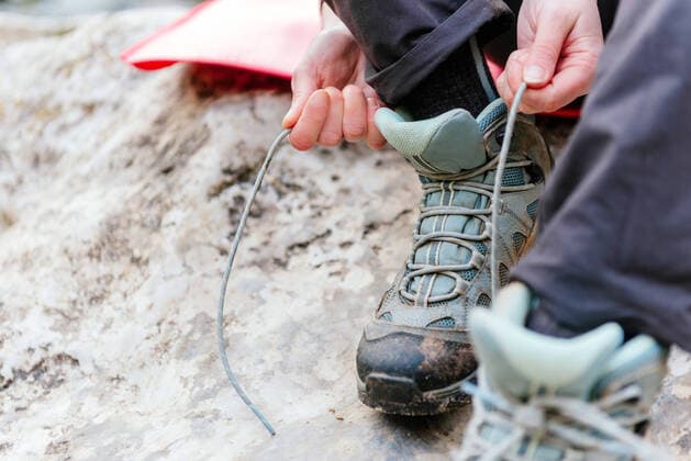 High angle of crop anonymous hiker tying shoelaces on sneakers for hiking in nature, Model released Copyright: xAlbertoxMenendezx MR
