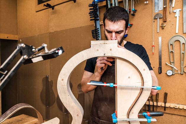 Male luthier artisan writing on wooden piece while making wooden musical instrument at table in workroom with manual tools Copyright: xLuisxManuelxMunozx Model Released