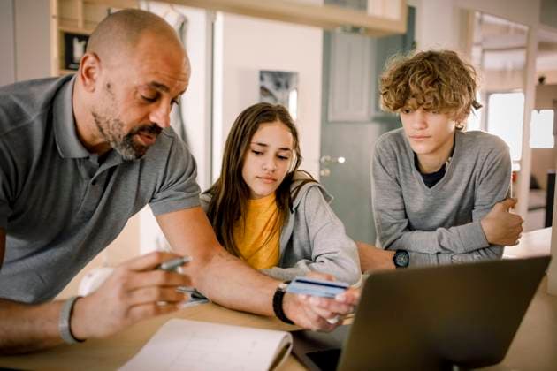 Brother and sister looking at father explaining finance with credit card at kitchen island Sweden, Stockholm, model released, property released Copyright: xMaskotx , MA86519
