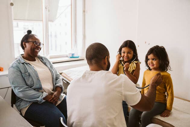 Smiling girl listening to sister s heartbeat while male doctor examining with stethoscope Sweden, Stockholm, model released, property released Copyright: xMaskotx , MA86789