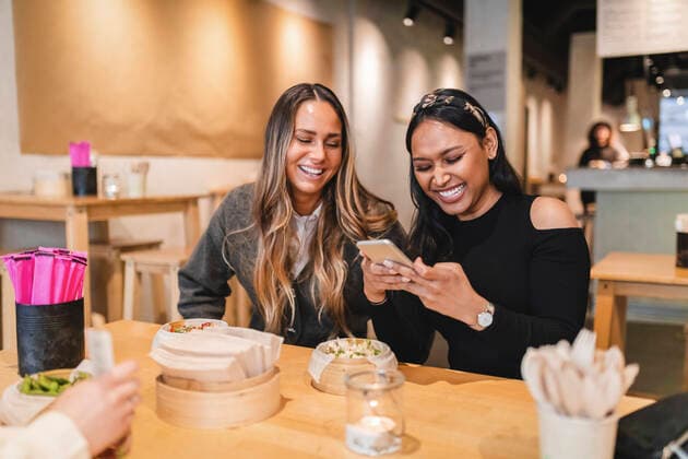 Smiling female friends using smart phone while sitting in restaurant Sweden, Gothenburg, model released, property released Copyright: xMaskotx , MA86814