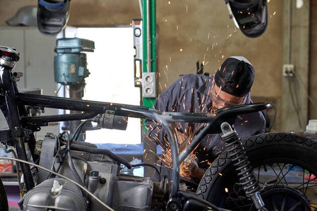 Bearded worker in overall using angle grinder while polishing metal details of custom motorcycle in workshop Copyright: xPhilippexDegrootex Model Released