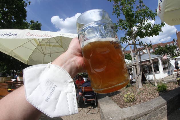 Due to low incidences in Würzburg, beer gardens were allowed to serve guests outside again A hand with FFP 2 mask on wrist holds up a mass of beer in the sunshine, Bavaria, Germany