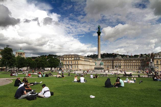 Despite the changeable weather and constant danger of thunderstorms many people sit on the green area at the Schlossplatz in front of the castle in the city center of Stuttgart, Baden Württemberg, Germany