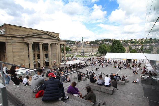 People sitting relaxed on the steps of the open staircase at the Schlossplatz in downtown Stuttgart, Baden Württemberg, Germany