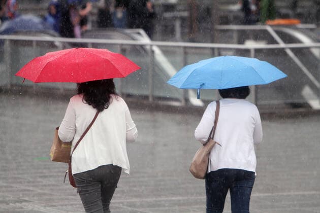 Two women walk with colorful umbrellas across the Schlossplatz in downtown Stuttgart during a heavy rainstorm, Baden Württemberg, Germany