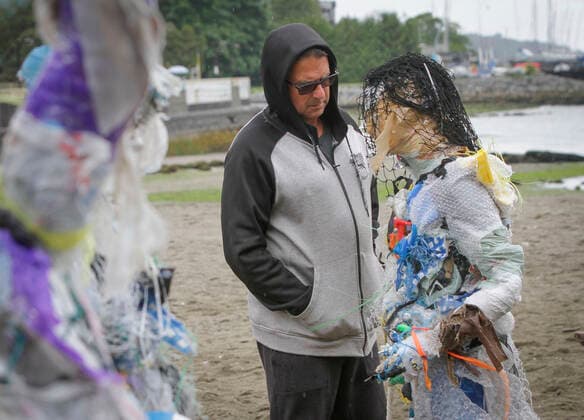 (210606) -- VANCOUVER, June 6, 2021 -- A man looks at a figure made with plastics removed from shorelines at Kitsilano Beach in Vancouver, British Columbia, Canada, on June 6, 2021. Created by multidisciplinary artist Caitlin Doherty and made with plastics removed from Canadian shorelines, a set of figures named plastic beachgoers embody people s collective contribution to plastic pollution, bring the topic of shoreline pollution to the forefront. (Photo by Xinhua) CANADA-VANCOUVER-INSTALLATIONS-PLASTIC BEACHGOERS LiangxSen 