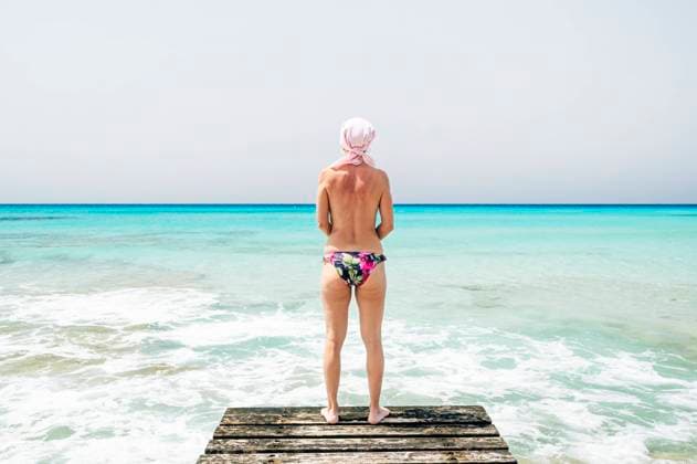 IMAGO Creative: Brustkrebsmonat Woman in swimsuit with pink scarf on the beach, has cancer Formentera, IB, Spain CR_TAXT210608-759446-01 ,model released, Symbolfoto