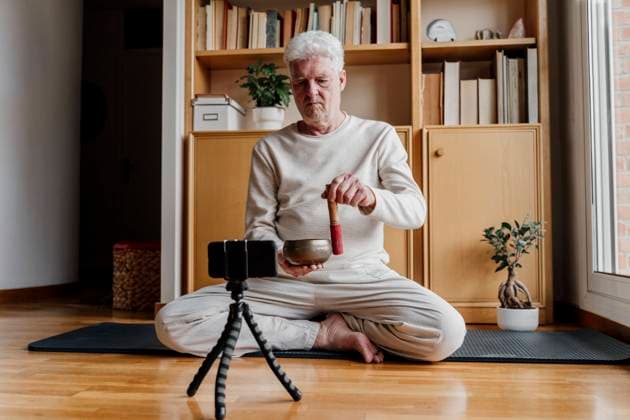 Male influener showing Tibetan Singing Bowl while vlogging through mobile phone at home model released Symbolfoto property released AFVF08784