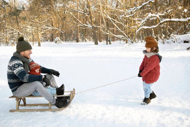 Son pulling father and younger brother sitting on sled during winter model released Symbolfoto FVDF00068