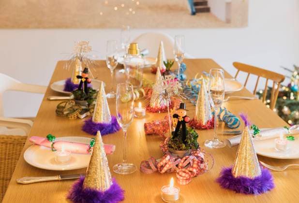 Festive laid New Years Eve table with plates, candles, party hats, champagne flutes and chimney sweep figurines property released GWF07001