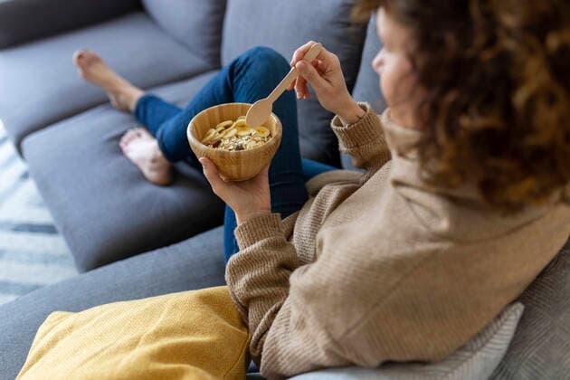 IMAGO Creative: Jahreszeit Winter, Couching Woman with food bowl in living room at home model released Symbolfoto property released JPTF00770