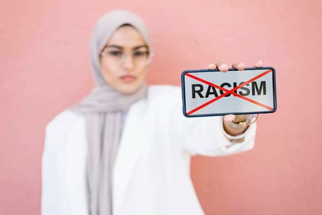 Young woman showing stop racism picture on smart phone in front of pink wall model released Symbolfoto property released XLGF01587