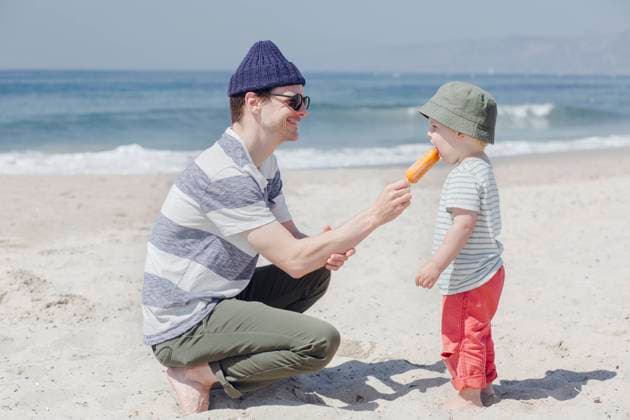 Smiling man feeding ice cream to son at beach during sunny day model released Symbolfoto ACTF00062