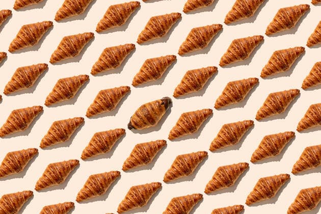 One chocolate croissant amidst butter croissants on beige background GEMF04796