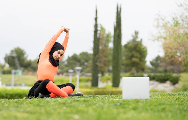 Young woman doing stretching while watching tutorial on laptop in park model released Symbolfoto JCCMF02588
