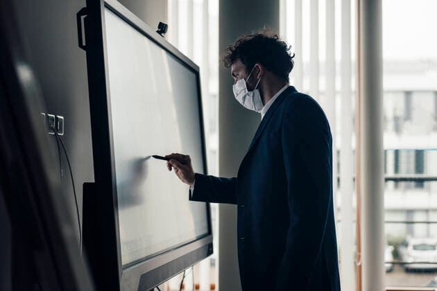 Male entrepreneur with face mask writing on projection screen in office model released Symbolfoto property released JOSEF04890