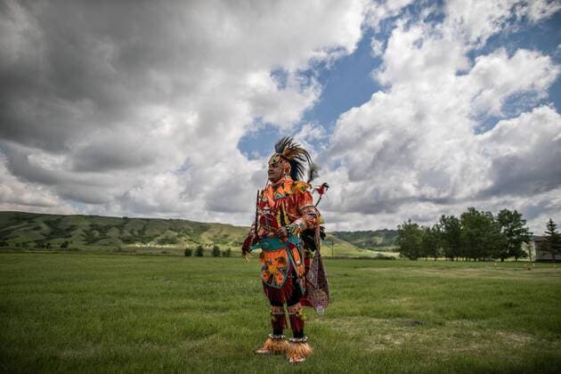 (210627) -- SASKATCHEWAN (CANADA), June 27, 2021 -- A member of the Cowessess First Nation stands in ceremonial outfit at the site of unmarked graves near a former indigenous residential school in Saskatchewan, Canada, on June 27, 2021. The Cowessess First Nation, an indigenous group in Saskatchewan, on Thursday announced a preliminary discovery of 751 unmarked graves near a former indigenous residential school. (Photo by Xinhua) CANADA-SASKATCHEWAN-UNMARKED GRAVES AmruxSalahuddien 