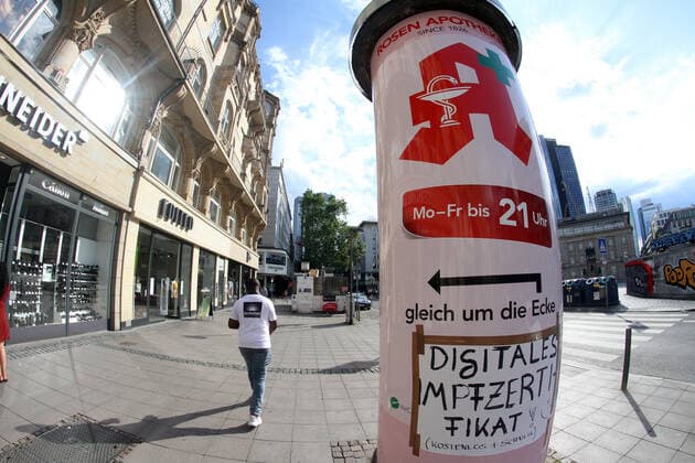 Sign saying digital vaccination certificate around the corner free and fast sticks to an advertising pillar in downtown Frankfurt, Hesse, Germany