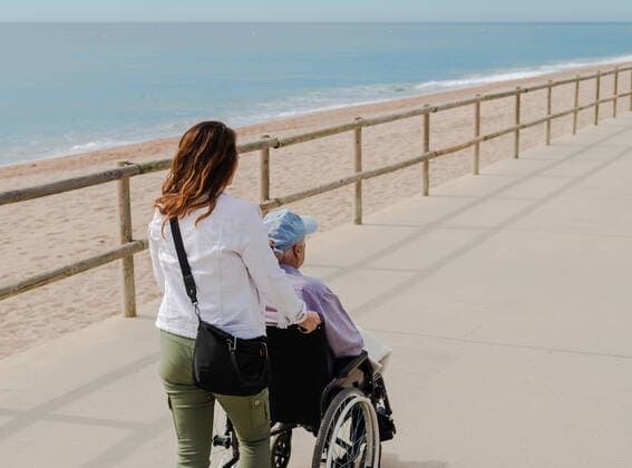 IMAGO Creative: NGO, Rehabilitation und Gesundheitswesen Delighted adult daughter pushing wheelchair with senior father and enjoying stroll along promenade near sea, Model released Copyright: xLuisxMarioxHernandezx MR