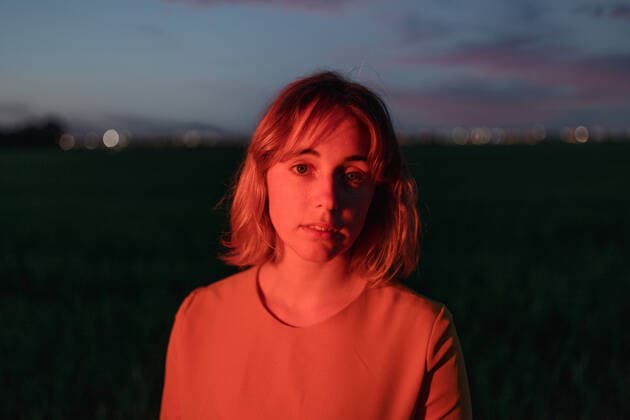 Dreamy young female in vintage style dress looking a camera thoughtfully while standing alone in dark grassy field against cloudy sundown sky in twilight AlbertoOrtega_VintageDressCountryside_54.jpg Copyright: xAlbertoxOrtegax Model Released