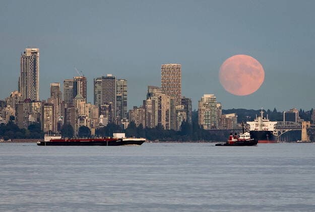 July 22, 2021, Vancouver, BC, Canada: A nearly full moon rises behind condo towers in the downtown skyline as a tugboat pulls a barge and a bulk carrier cargo ship sits at anchor on English Bay, in Vancouver, on Thursday, July 22, 2021. Vancouver Canada  - ZUMAc35_ 20210722_zaf_c35_041 Copyright: xDarrylxDyckx