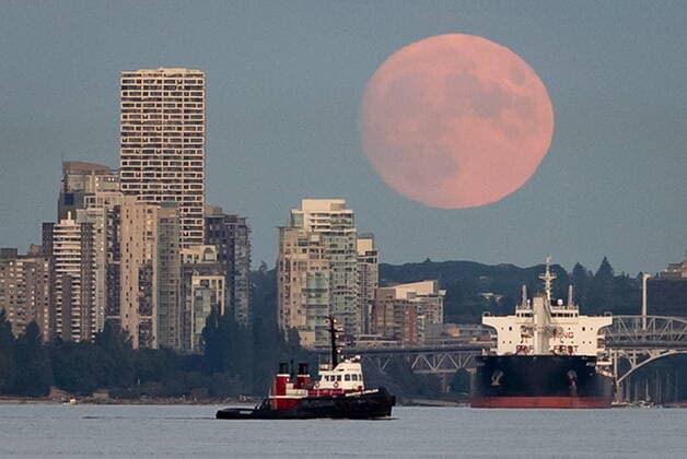 July 22, 2021, Vancouver, BC, Canada: A nearly full moon rises behind condo towers in the downtown skyline as a tugboat pulls a barge and a bulk carrier cargo ship sits at anchor on English Bay, in Vancouver, on Thursday, July 22, 2021. Vancouver Canada  - ZUMAc35_ 20210722_zaf_c35_043 Copyright: xDarrylxDyckx